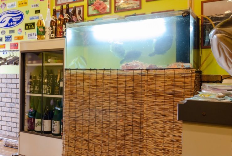 飲食店内に設置された大型水槽と酒瓶が並ぶ冷蔵庫の風景
