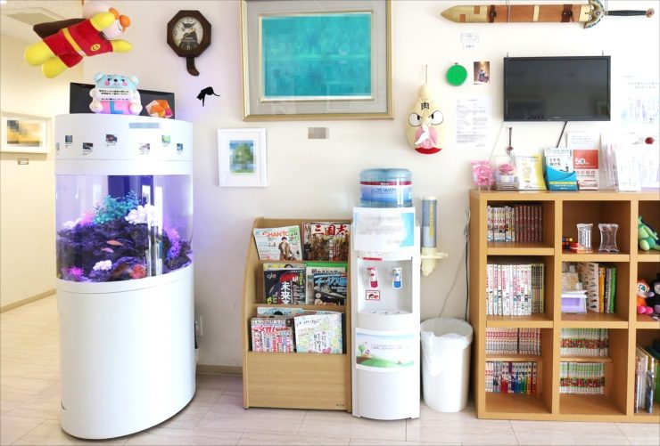 待合室に設置された円柱型水槽と本棚のある風景
