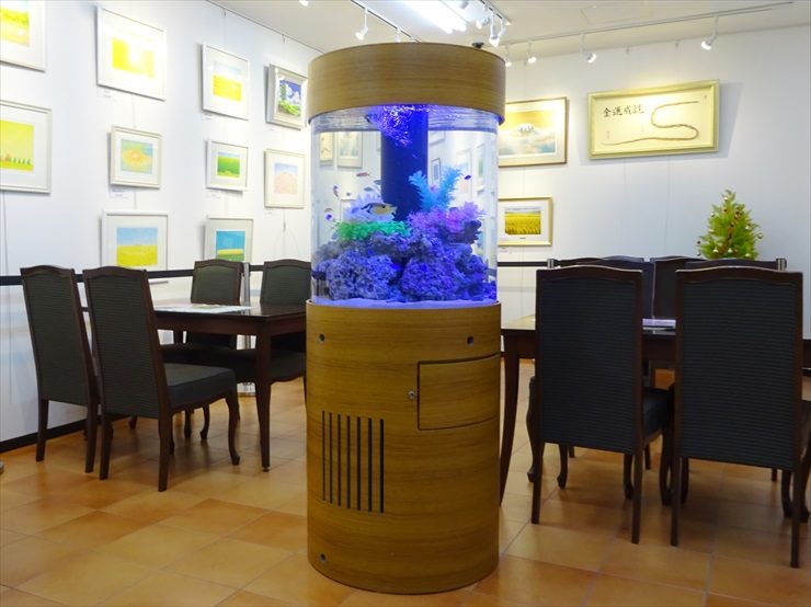 絵画が飾られた室内に置かれた円柱型水槽