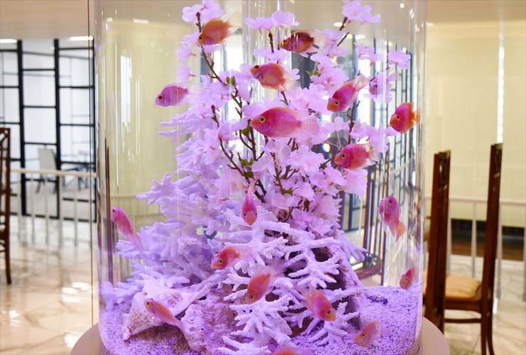 円柱水槽を泳ぐピンク色の熱帯魚と桜の造花装飾