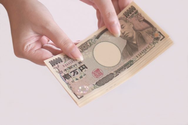 両手で持った一万円札の束と福沢諭吉の肖像画