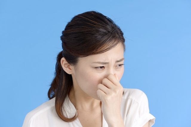 青い背景の前で鼻をつまみ顔をしかめる女性の姿