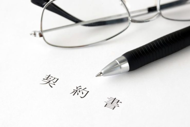 契約書と書かれた書類の上に置かれたペンと眼鏡