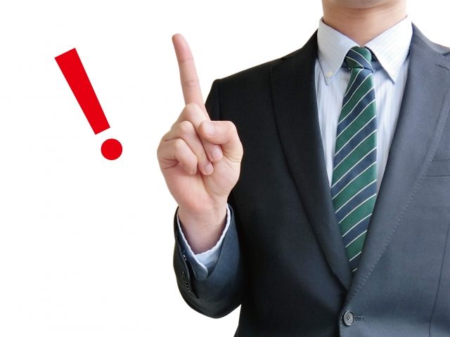 人差し指を立てるスーツ姿の男性と赤いビックリマーク
