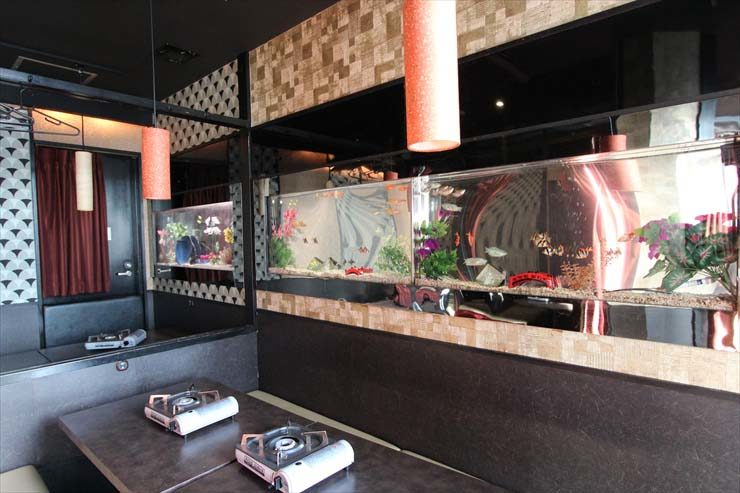 飲食店内の壁面に埋め込まれた横長の水槽とテーブル席