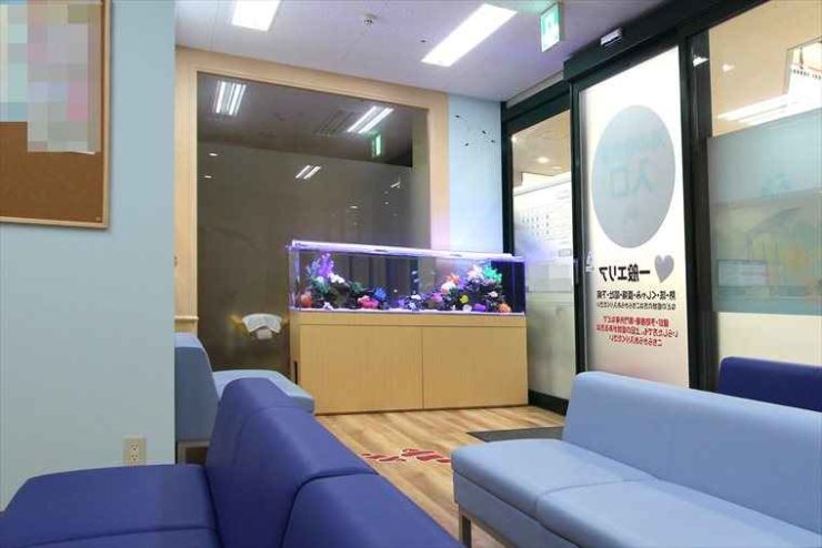 青いソファが並ぶ待合室に設置された大型海水魚水槽
