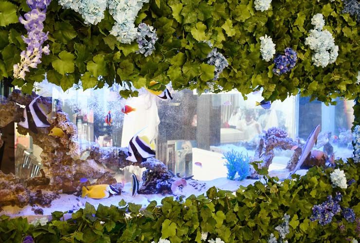 造花に囲まれた海水魚水槽と泳ぐ熱帯魚の群れ