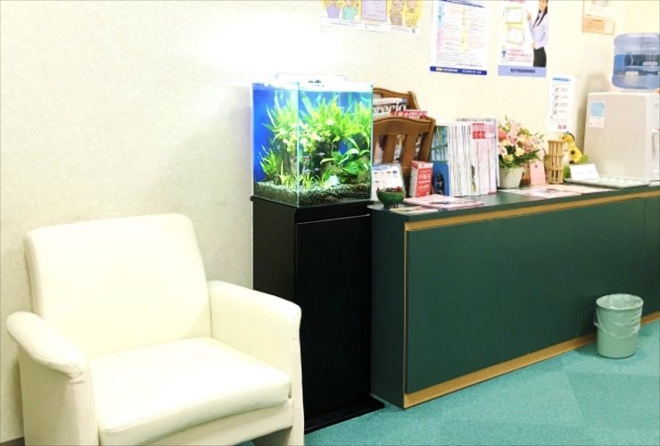待合室のソファ横に設置された小型水草水槽と黒い水槽台