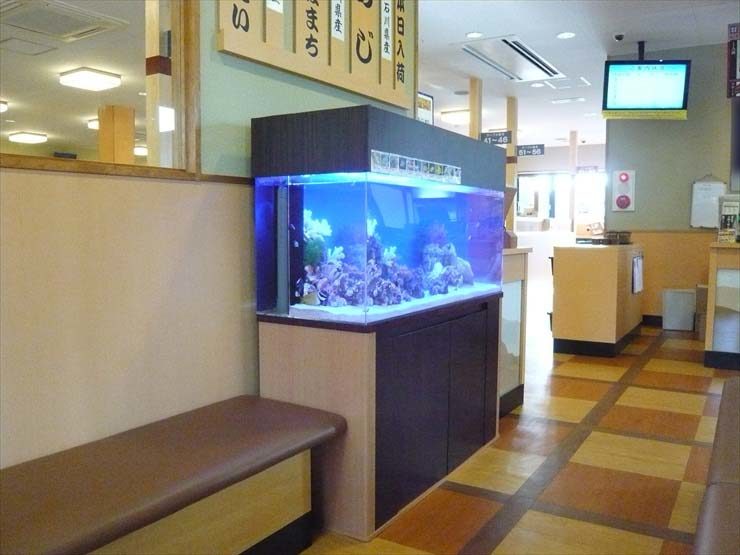 飲食店内に設置された大型の海水魚水槽と待合席の風景