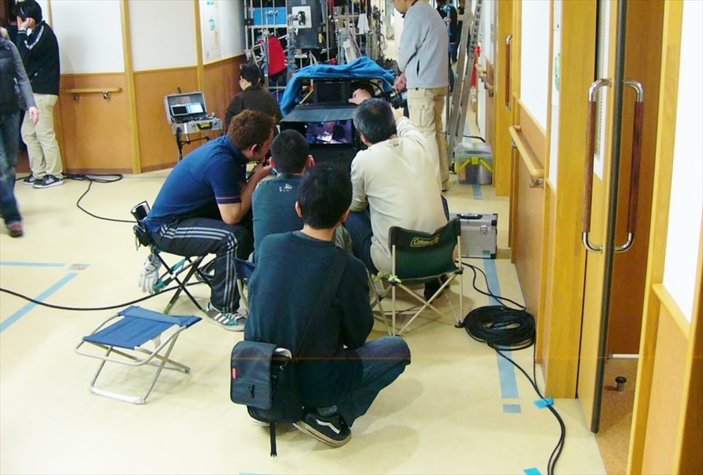 機材を囲みモニターを確認する撮影スタッフの背中