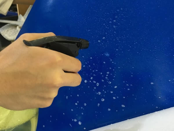 青色の水槽バックスクリーンに霧吹きで水をかける手元