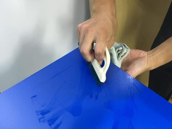 青いバックスクリーンをヘラで水槽に貼り付ける手元