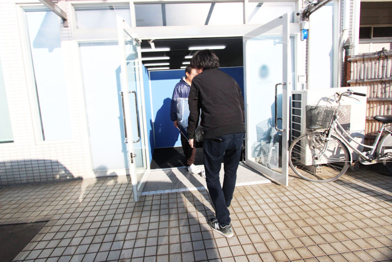 建物の入り口で荷物を運び出す二人の男性と自転車