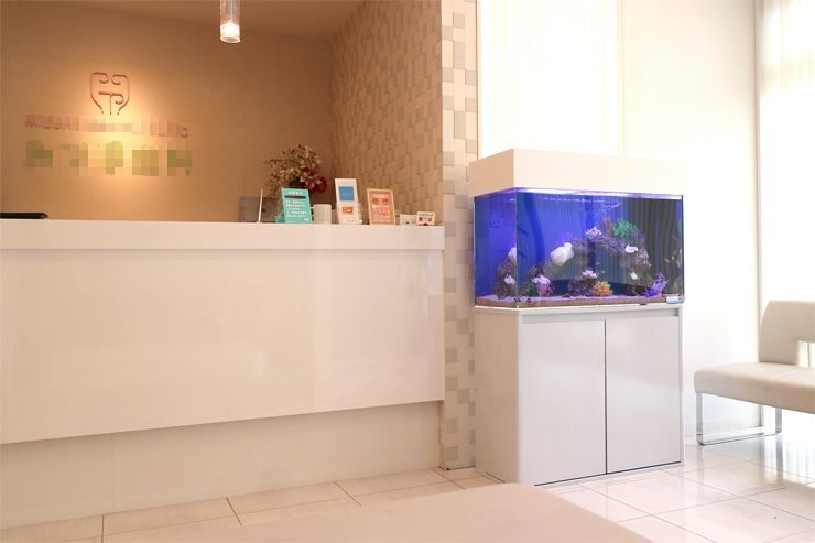 クリニック受付に設置された青い海水魚水槽と白いカウンター