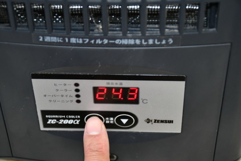 水槽用クーラーの温度設定ボタンを押す指先