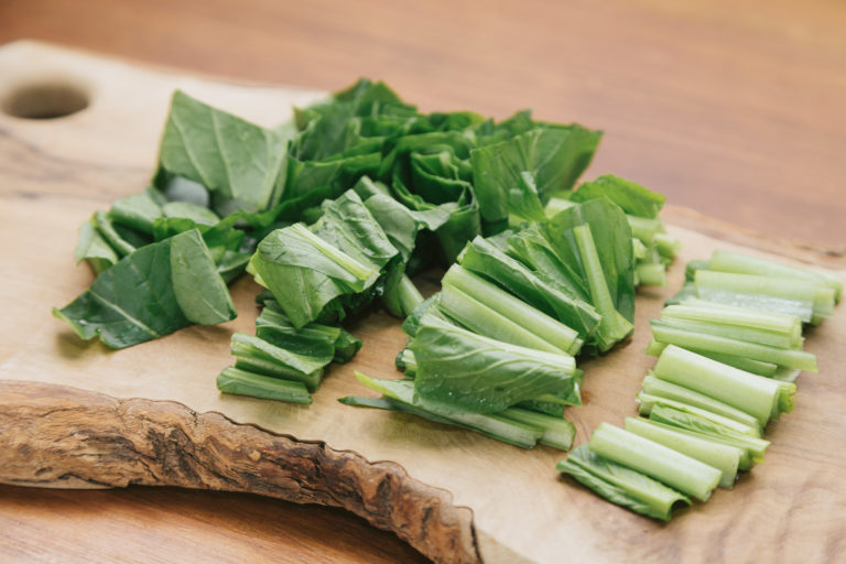 木製まな板の上でざく切りにされた緑色の葉物野菜