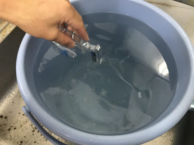 青いバケツに溜めた水と比重計を持つ人の手