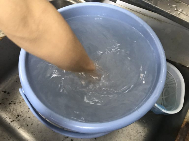 青いバケツに溜めた水を腕でかき混ぜる様子