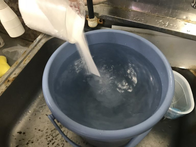 青いバケツの水に白い粉末を投入するシンク内の風景