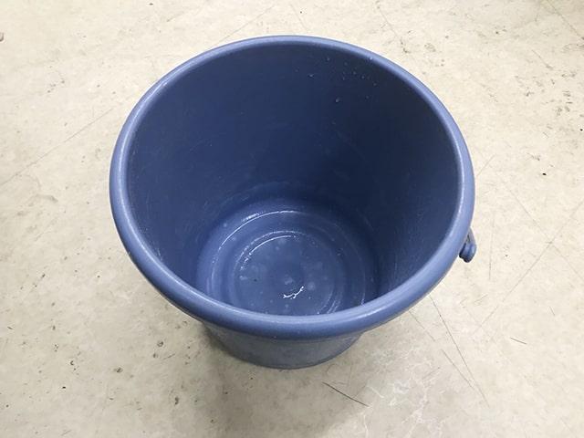 床の上に置かれた空の青いプラスチック製バケツ