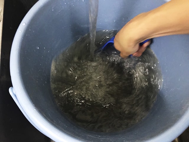 青いバケツに注がれる水と手を使いかき混ぜる水流