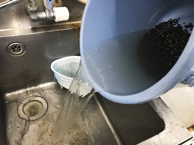 バケツに入れた底砂をシンクで水洗いする様子