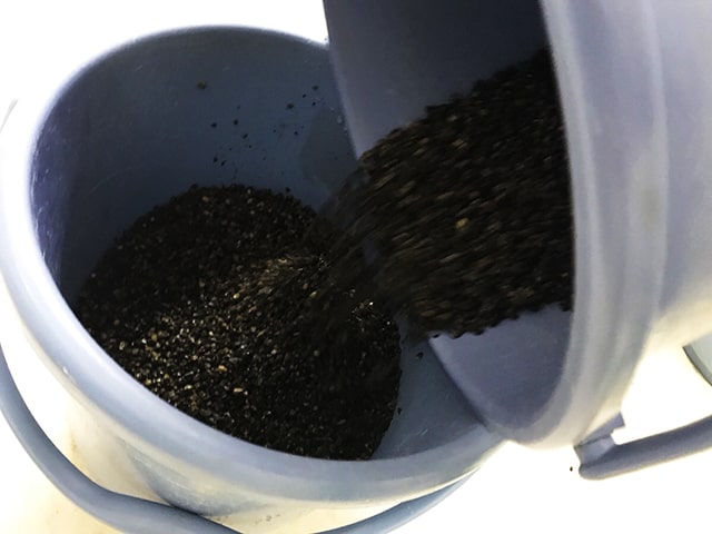 青いバケツから別のバケツへ移し替えられる黒い底砂