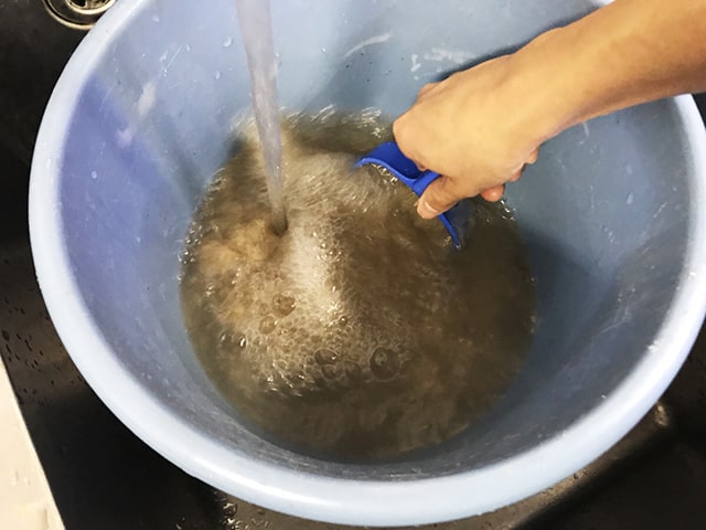 青いバケツで水槽用の砂利を水洗いする手元