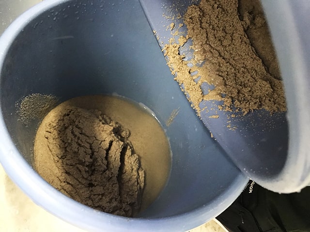 青いバケツに入れた水槽用の砂と洗浄中の濁った水