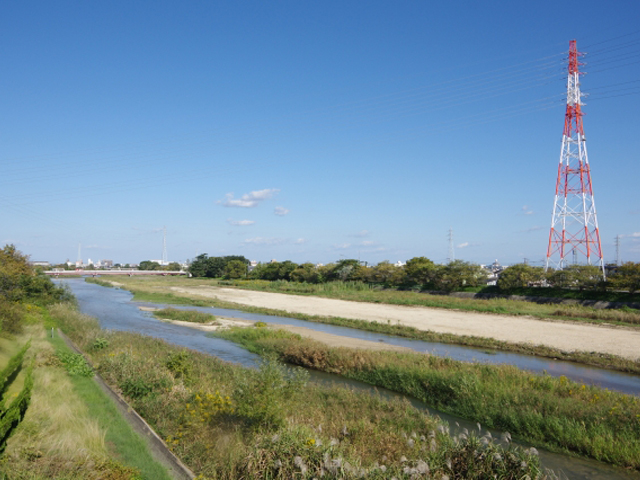 青空の下を流れる河川敷と紅白の送風鉄塔の風景