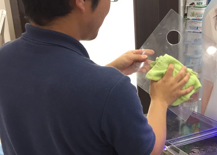 タオルでアクリル製の水槽の蓋を拭く男性の背中