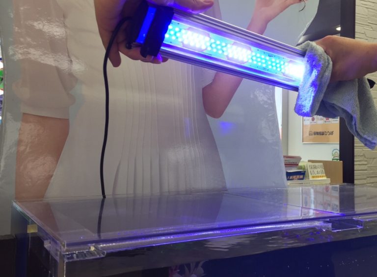 青白く点灯する水槽用LEDライトを布で拭く手元