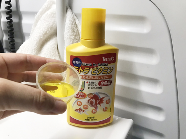 計量カップに入れた金魚用ビタミン剤の黄色い液体