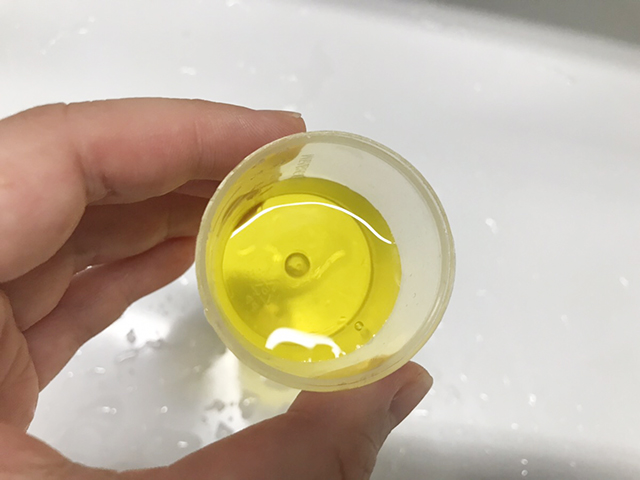 黄色い液体が入った計量カップを持つ手元
