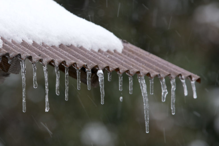 雪が積もった波板の屋根から垂れ下がる複数のつらら