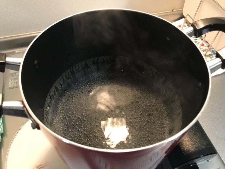 コンロ上の黒い両手鍋で沸騰するお湯と立ち上がる湯気