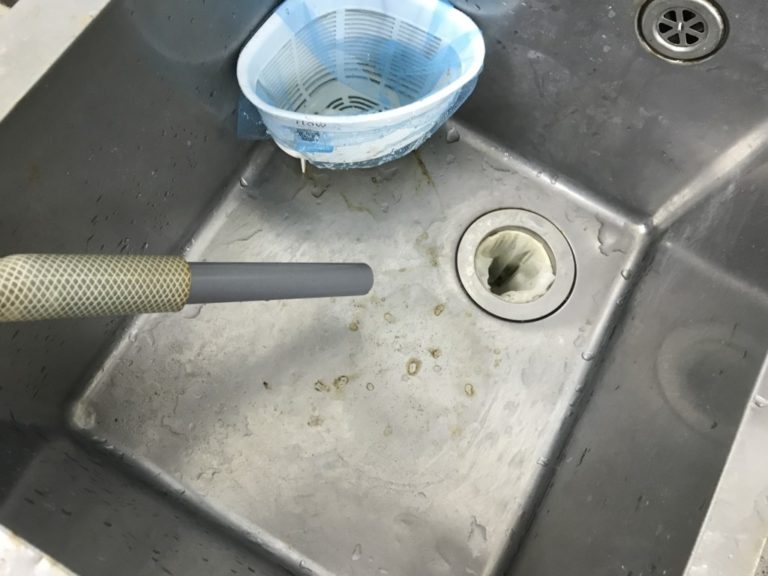 ステンレスシンクに向けられた給排水用ホースと水受けカゴ