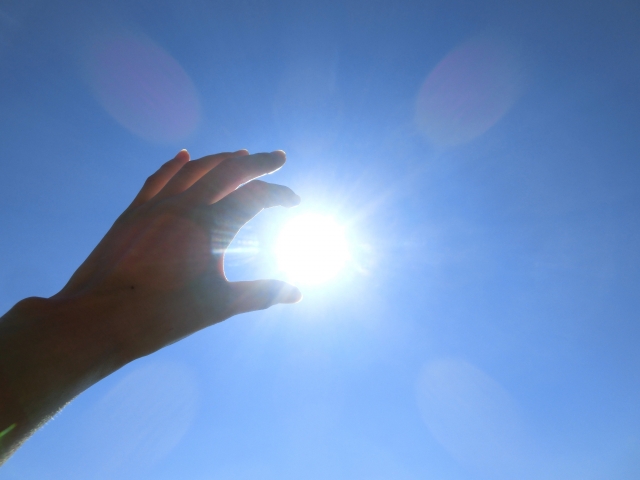 青空の下で太陽を掴むようにかざした人の手