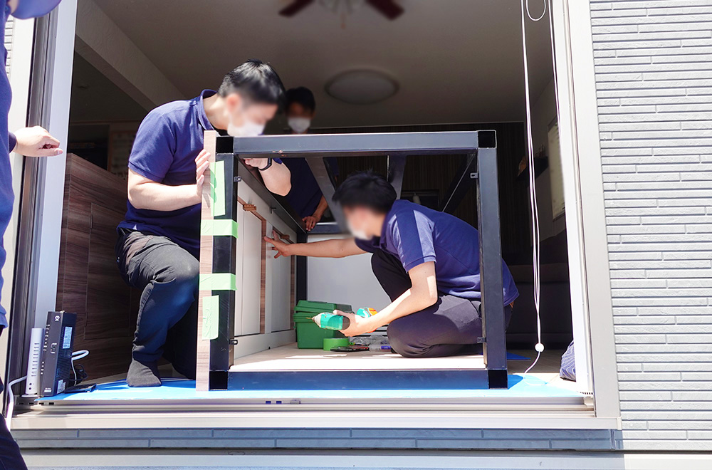 室内で黒い大型水槽台を組み立てる作業スタッフの姿
