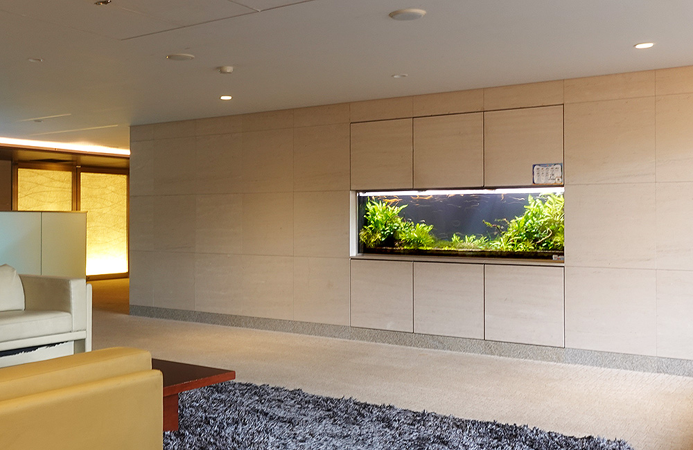 壁面に埋め込まれた水草の生い茂る大型水槽とロビーの風景