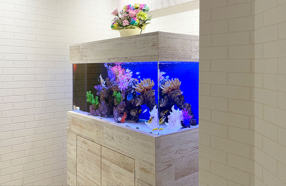 木目調の台に設置された海水魚水槽と上部のフラワーアレンジメント