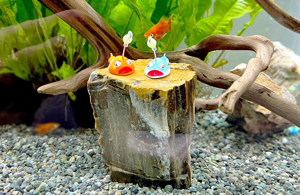 石の上の魚の置物と泳ぐメダカと水草の水槽内景観