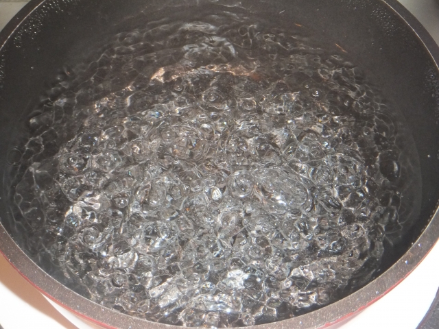 黒い鍋の中で激しく沸騰するお湯の気泡