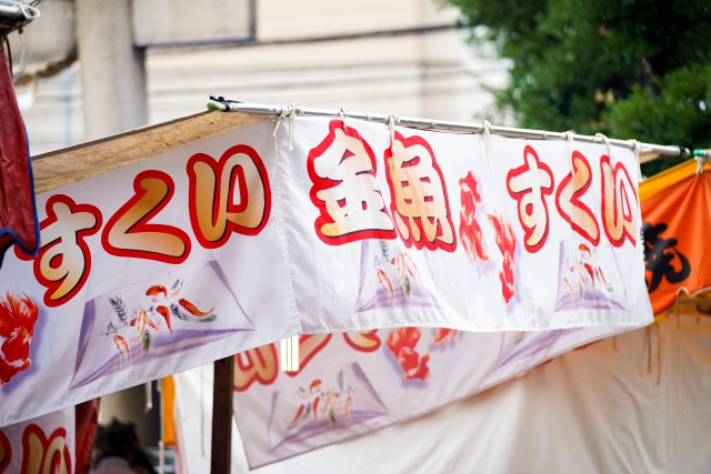 金魚すくいと書かれた縁日の屋台の白い看板幕