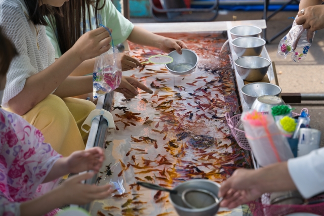 縁日の屋台で金魚すくいを楽しむ子供たちと水槽の金魚