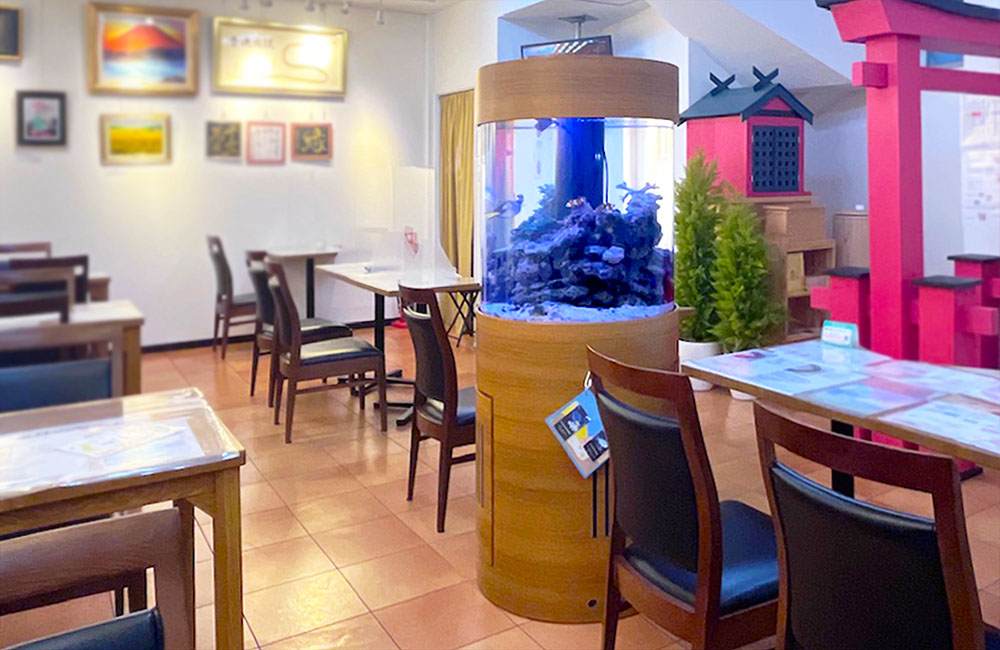 飲食店内に設置された円柱型の海水魚水槽と店内の風景