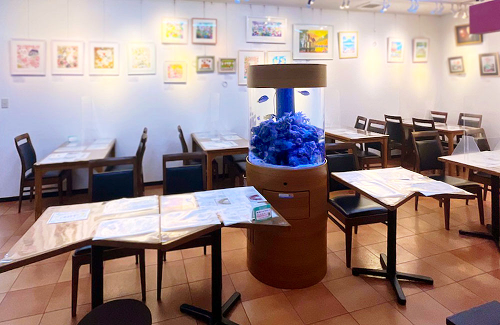 飲食店内に設置された円柱型の海水魚水槽と客席の風景