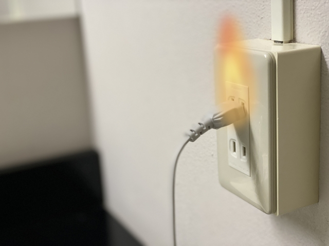 壁のコンセントに挿した電源プラグから上がる火花と炎