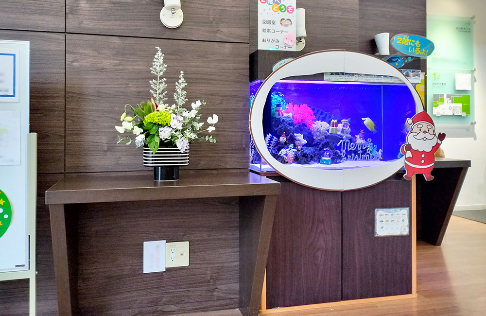 クリスマス装飾の海水魚水槽と隣に並ぶフラワーアレンジメント