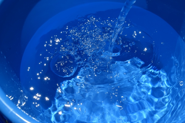 青いバケツに注がれる水と水面に浮かぶ気泡